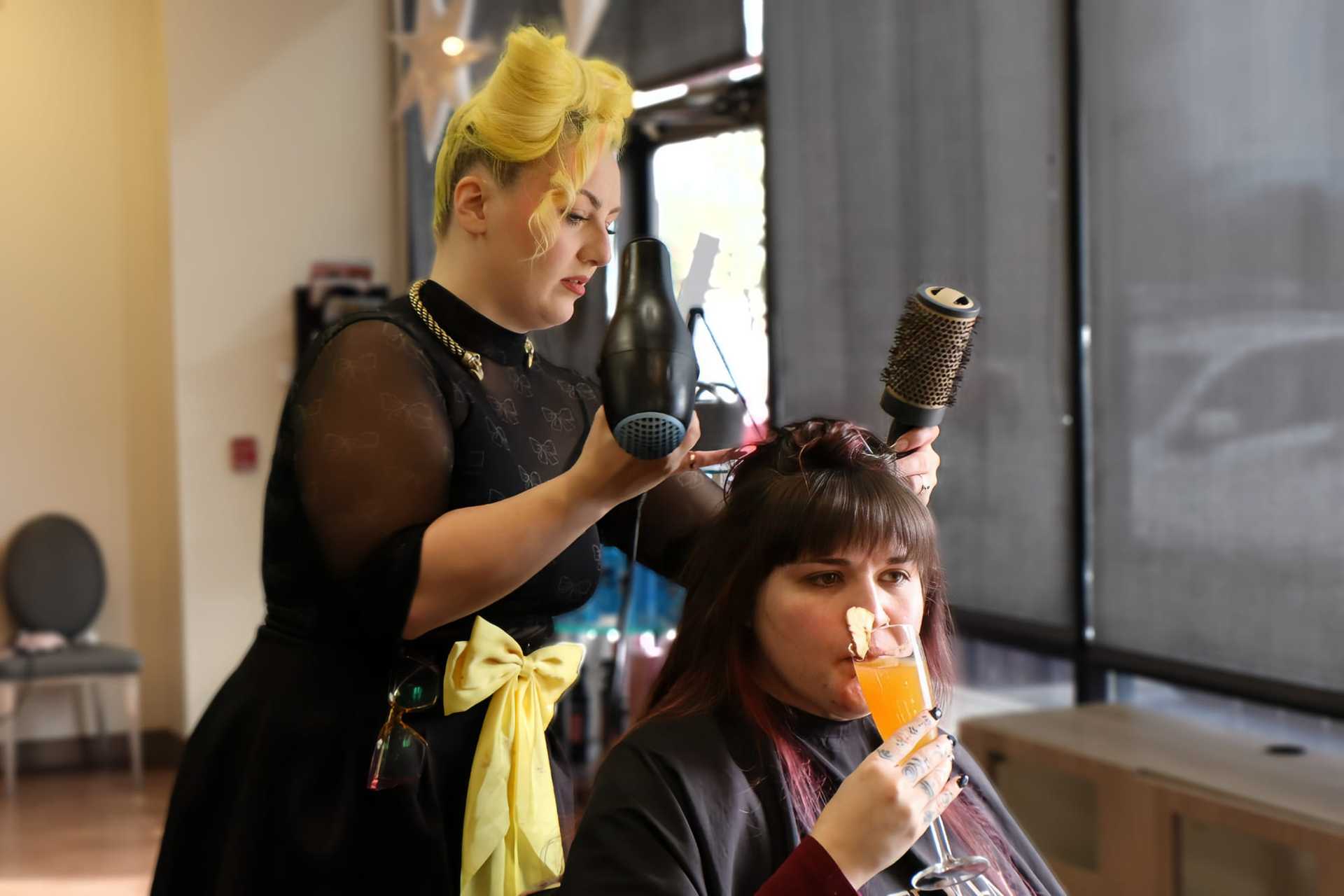 Woman getting hair styled while sipping a drink in a salon.