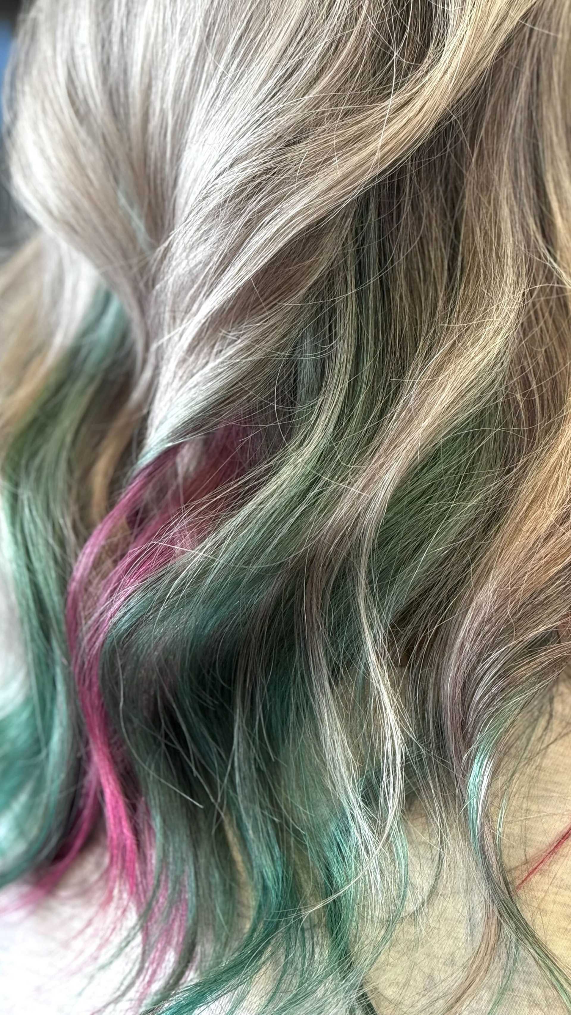 Wavy hair with blonde highlights and vibrant pink and green streaks.