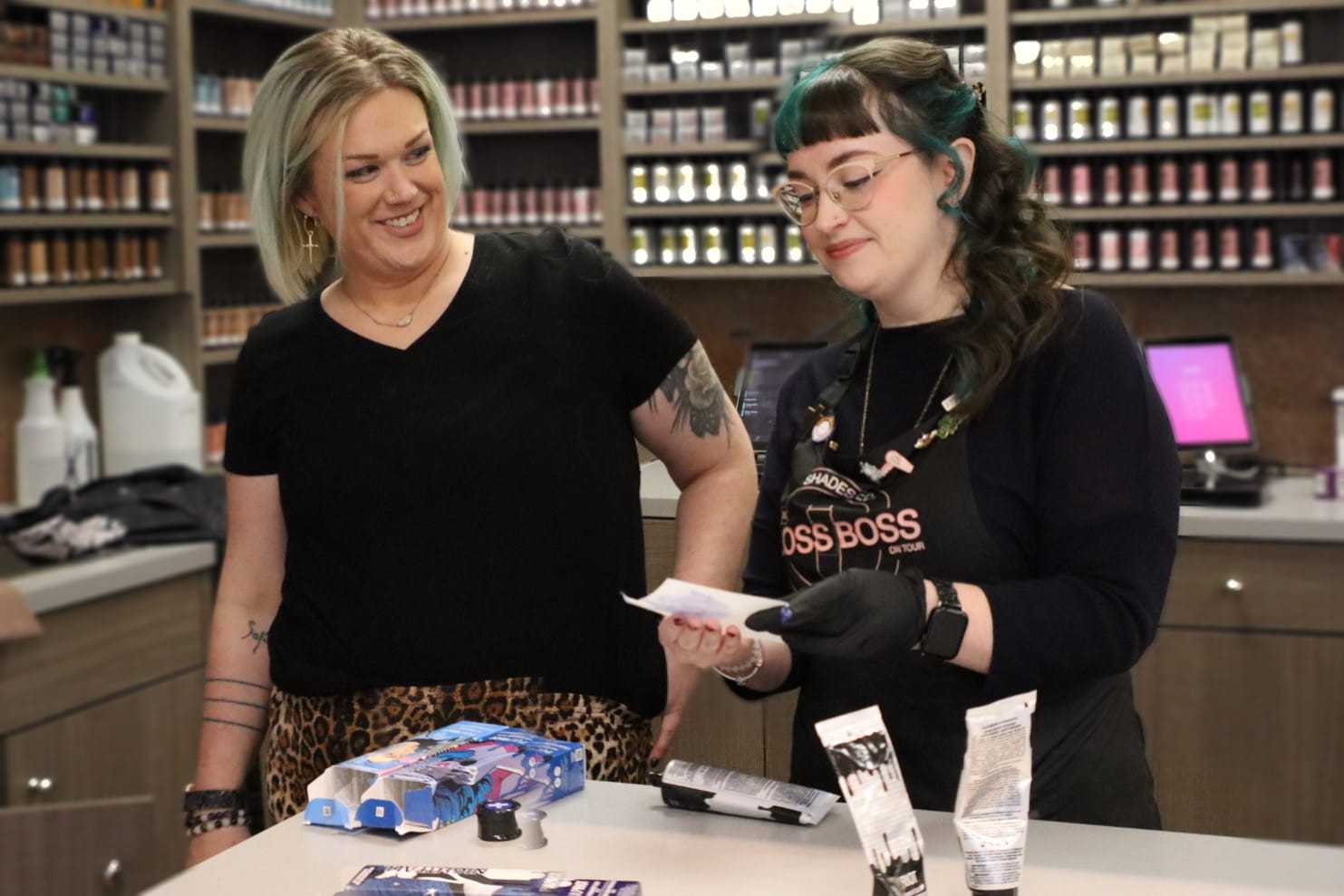 Two women discussing hair products at a counter in a salon.